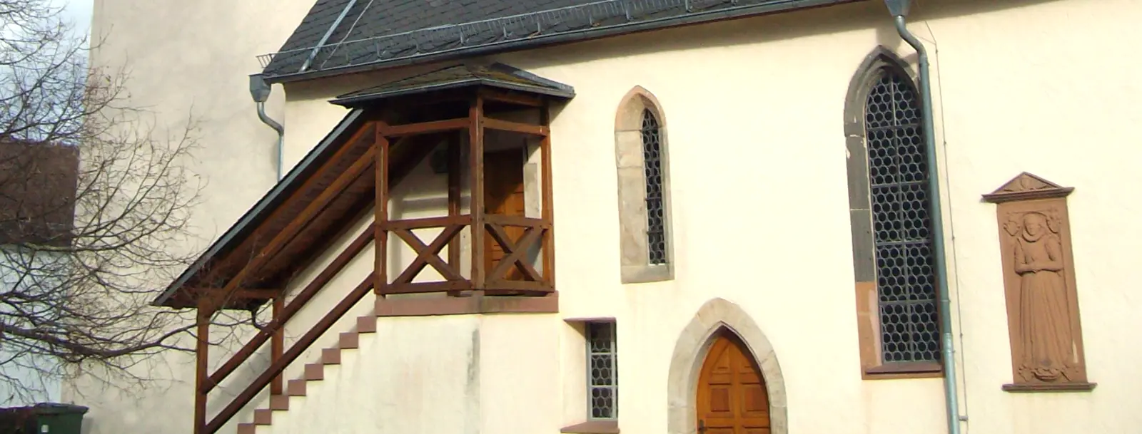 Weiße Kirchenmauer mit Fenstern und Treppe mit Holzgeländer und Überdachung