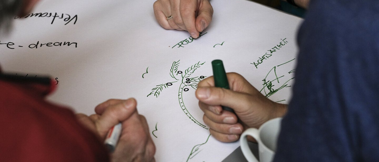 Mehrere Männer sitzen an einem Tisch und beschriften ein Plakat.