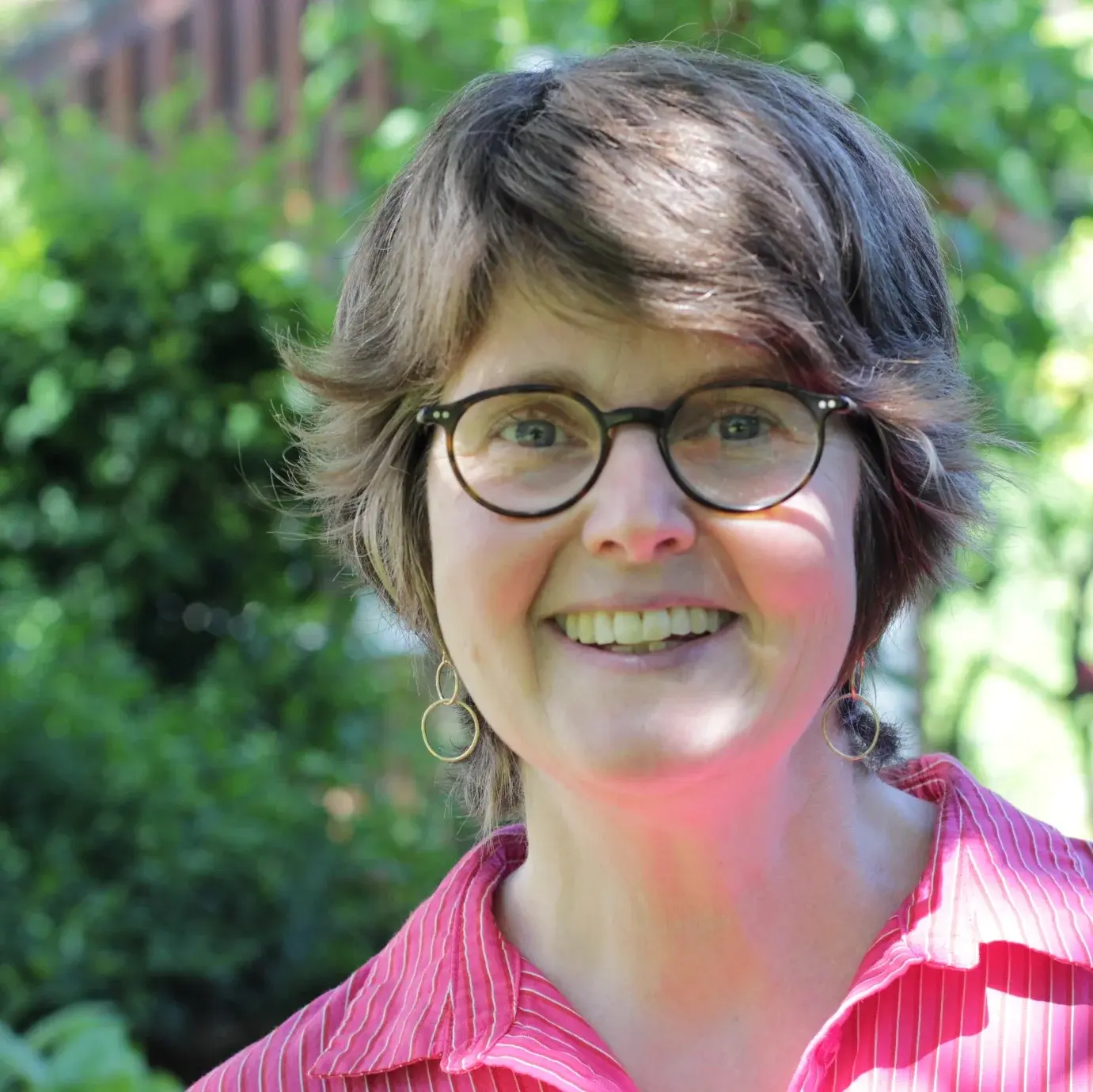 Porträt von Pfarrerin Bianca Schamp. Im Hintergrund unscharf grüne Blätter in einem Garten. 