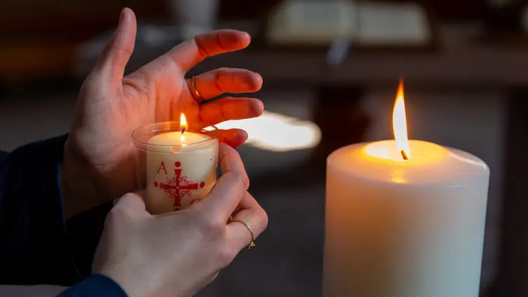 Jemand zündet eine Kerze an der Osterkerze in einer Kirche an.