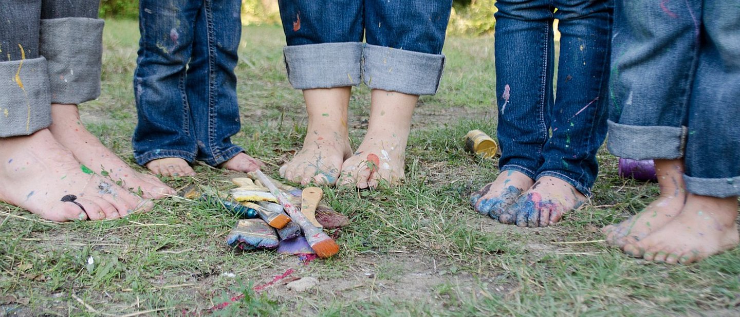 mehrere barfüßige Füße, klein und groß man sieht noch hochgekrempelte Jeanshosen. Sie stehen auf der Grünen Wiese