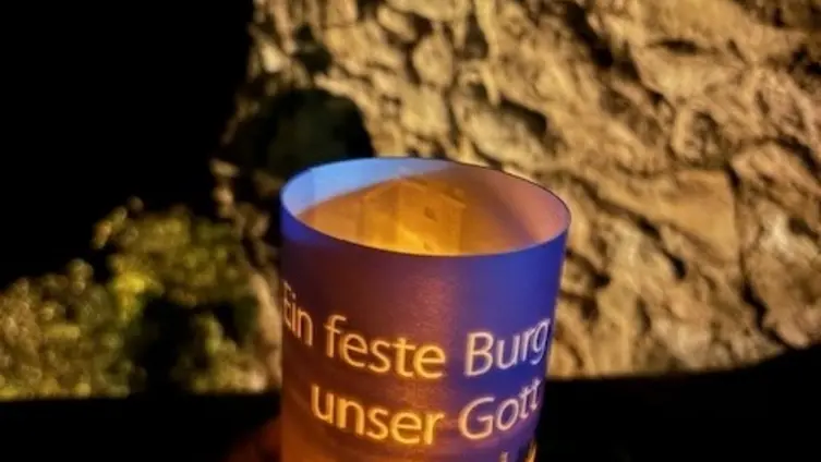 Es ist dunkel. Eine Hand hält ein kleines Licht mit einem Transparent und der Aufschrift: Ein feste Burg ist unser Gott