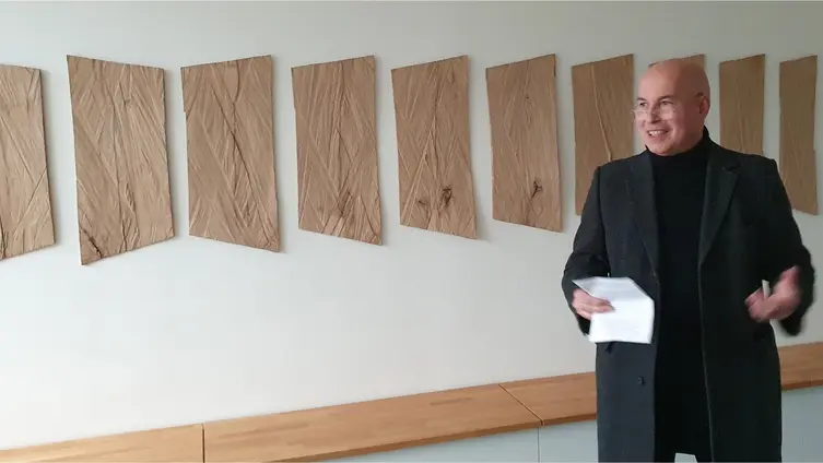 Der Pfarrer steht vor dem Kunstwerk an der Wand