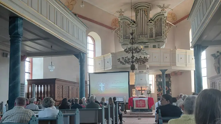 Das Foto zeigt viele Gottesdienstbesucher, im Hintergrund sind der Altarraum und eine Leinwand zu sehen.