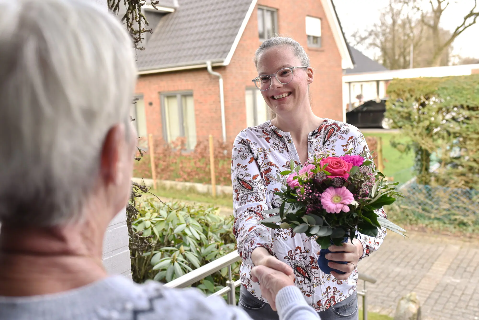 Eine Besucherin steht mit Blumenstrauß vor der Tür