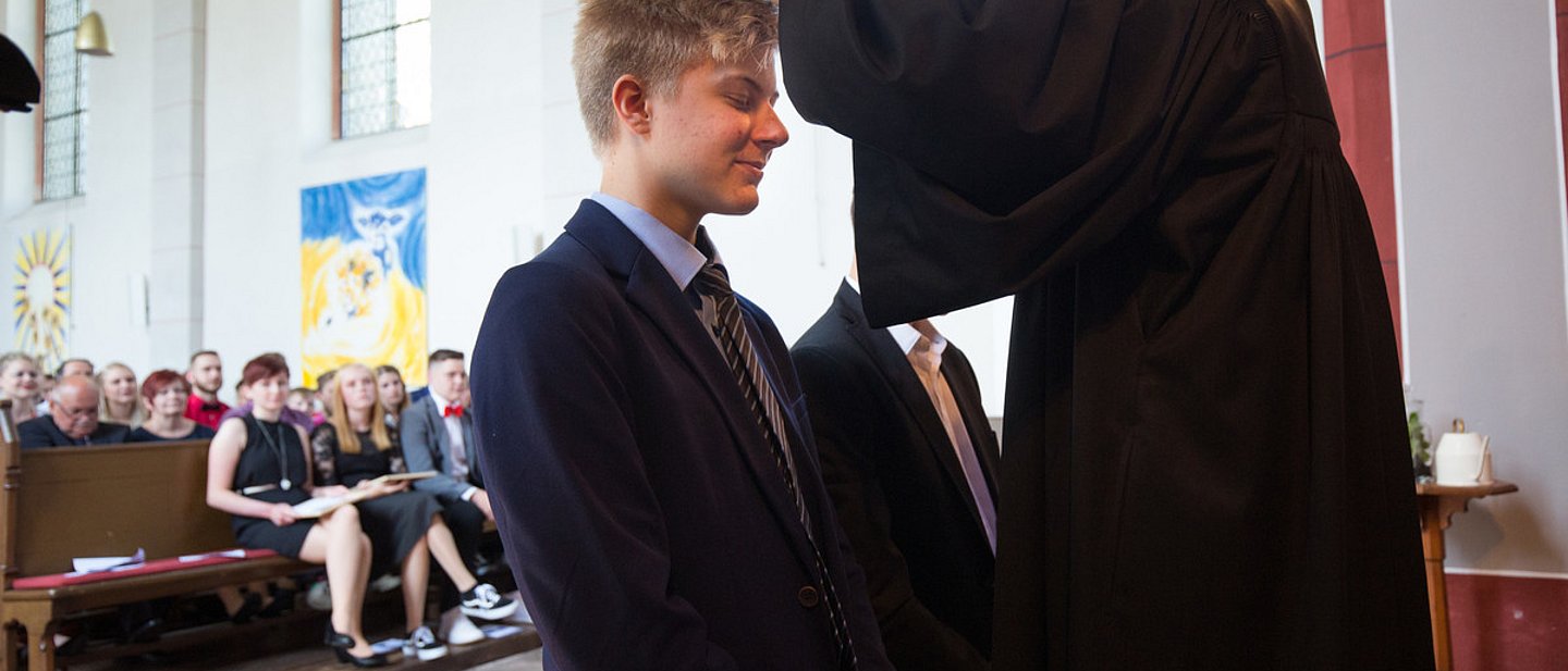 Eine Pfarrerin segnet zwei Konfirmanden