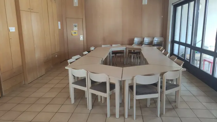 Eine Tischgruppe steht inmitten eines gefließten Raums. Links sind Schränke, rechts ist eine Schiebeglastür zu sehen