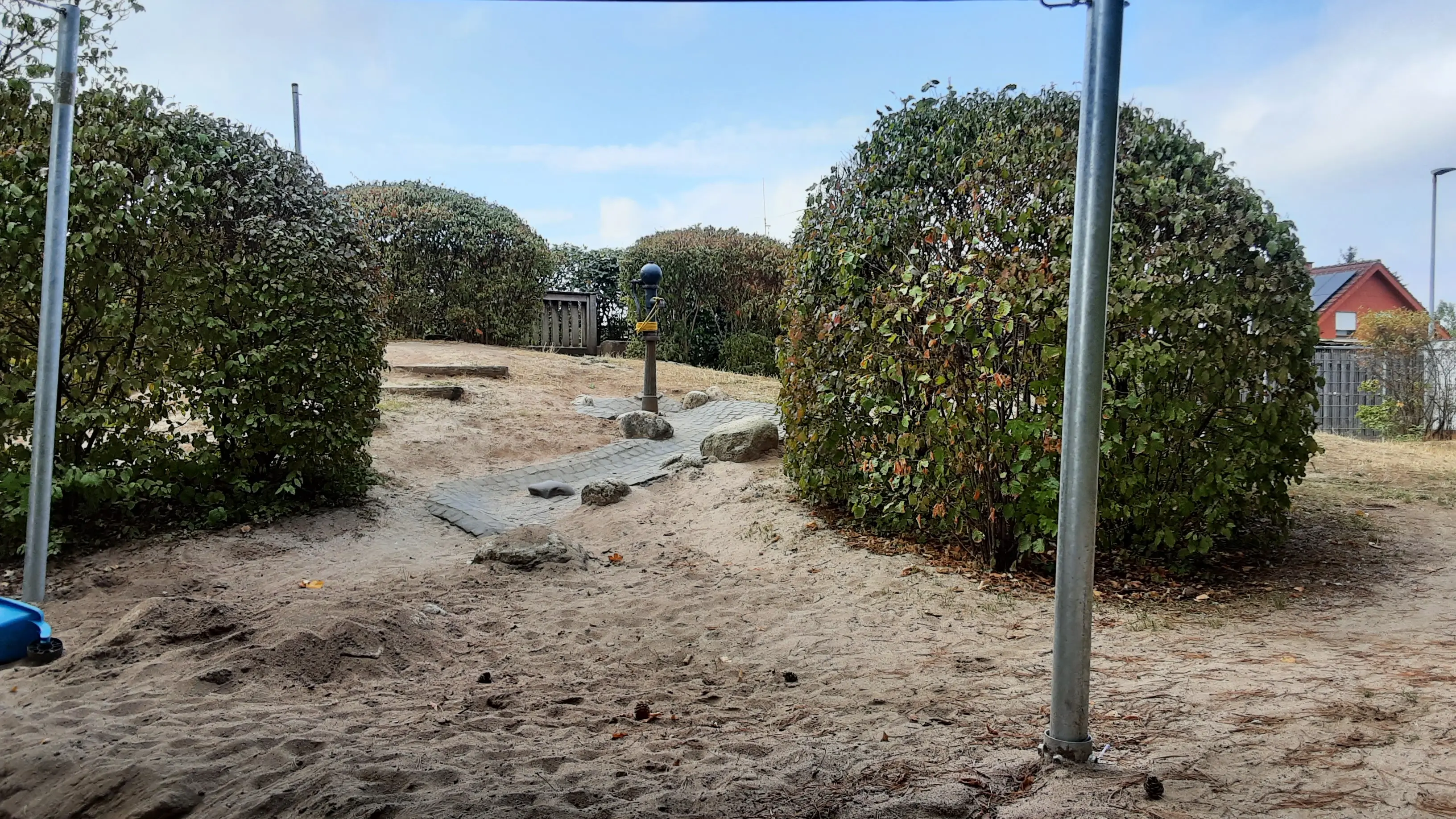Bild unserer Wasserpumpe, in dwer Mitte des Bildes, rechts und links davon sind Gebüsche, in der Mitte des Bildes verläuft der Wasserlauf.