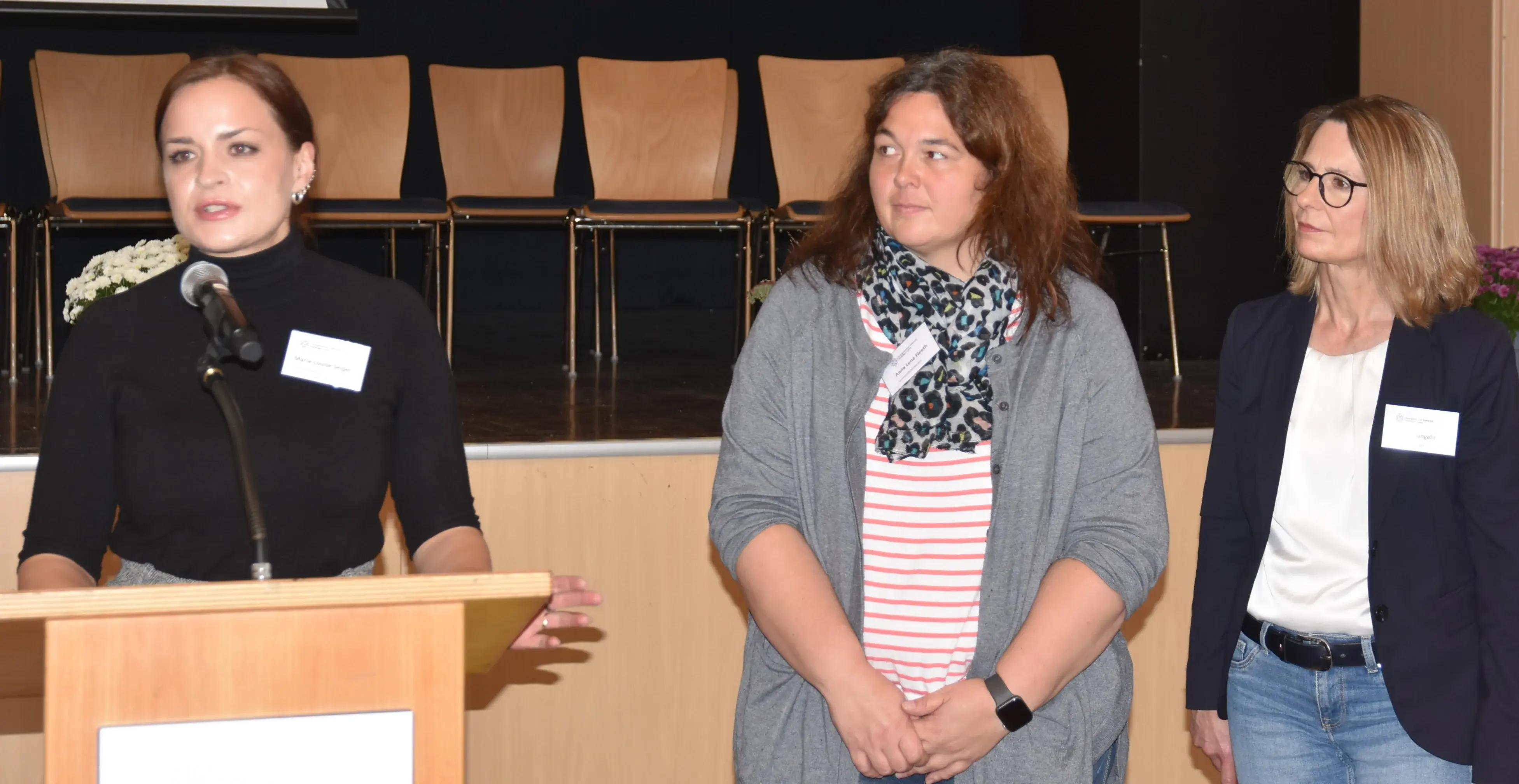Maria-Louise Seipel, Anna Lena Fleeth und Marion Gengel-Knapp stehen nebeneinander am Rednerpult vor der Bürgerhaus-Bühne in Nidda.