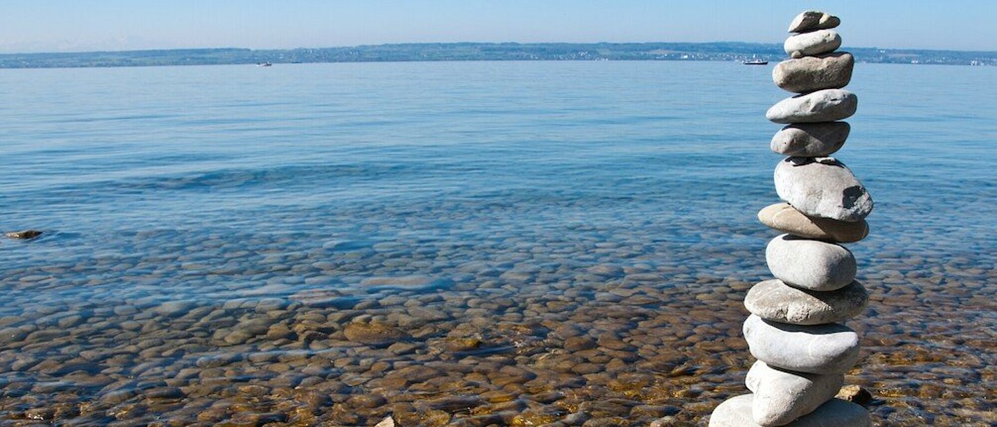 Mehrere runde, weiße Steine wurden zu einem Steinturm gestapelt. Im Hintergrund der Bodensee