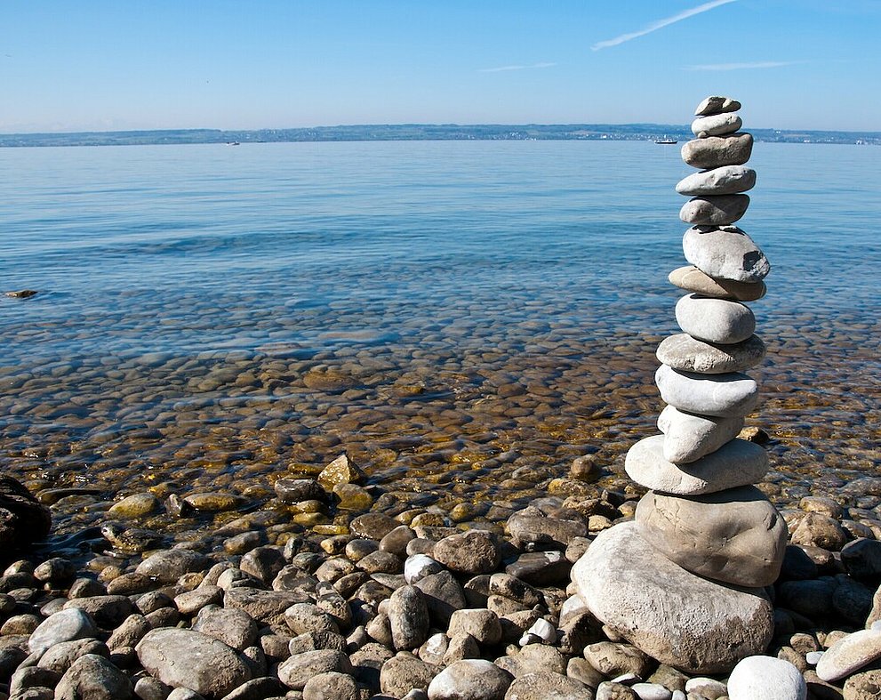 Mehrere runde, weiße Steine wurden zu einem Steinturm gestapelt. Im Hintergrund der Bodensee