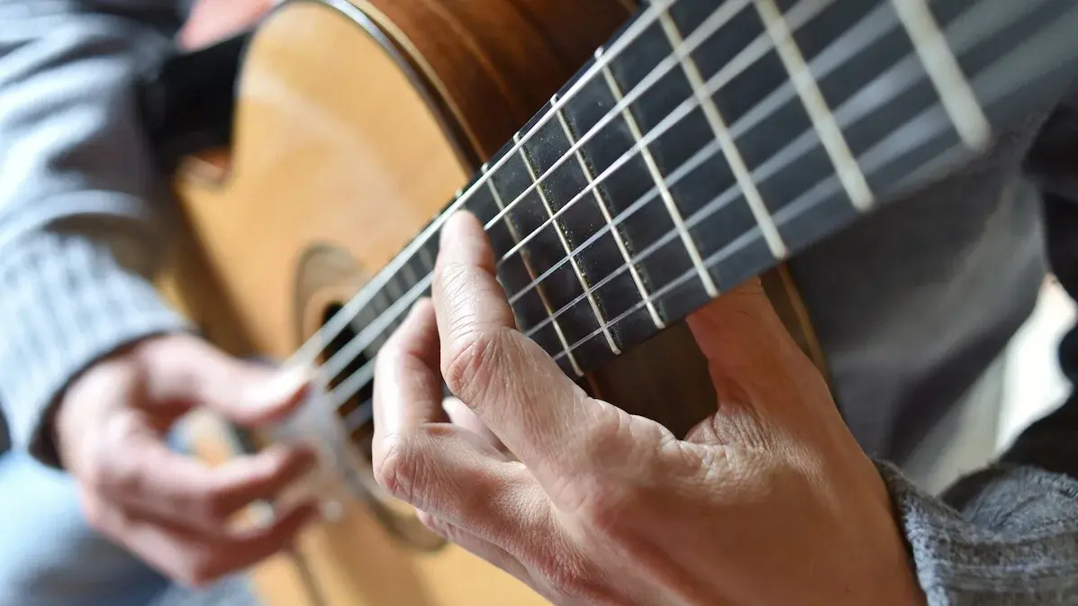 Nauaufnahme einer Person, die Gitarre spielt. Man sieht die Hände und die Gitarrenseiten.