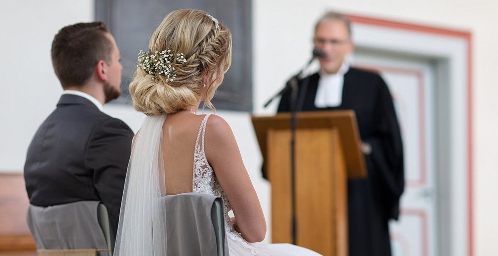 Ein bRautpaar bei der Trauung mit derm Pfarrer in der Kirche