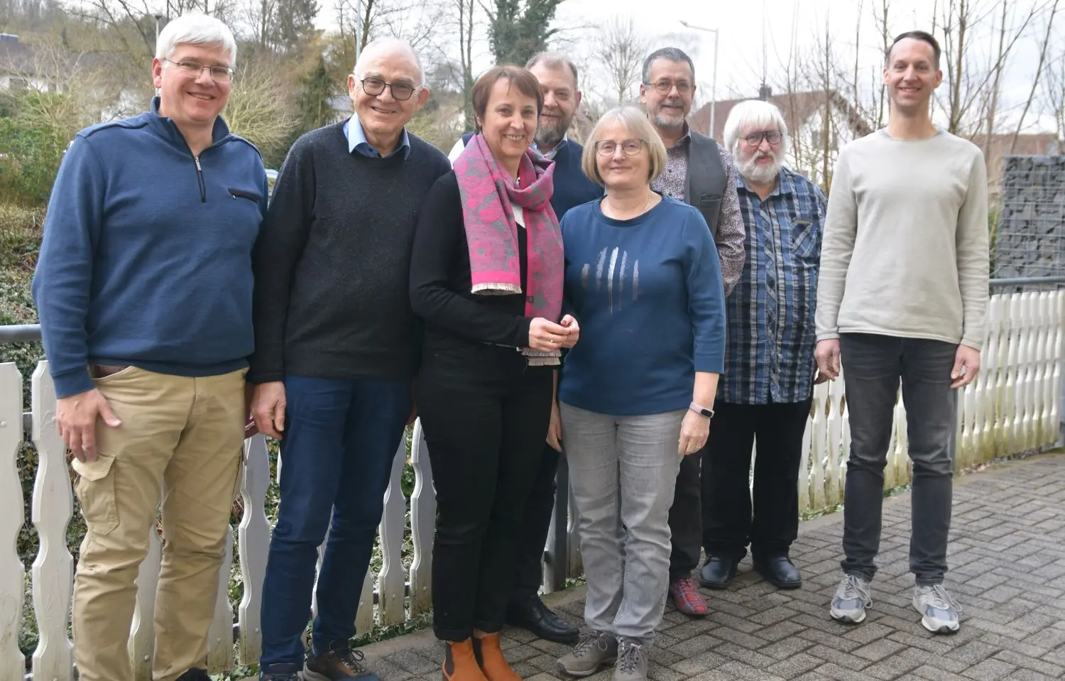 Aufnahme im Freien, herbstlicher/winterlicher Hintergrund, sechs Männer und zwei Frauen stehen in einer Gruppe nebeneinander.