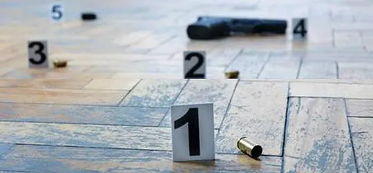 Auf dem Boden liegen Patronenhülsen und eine Schusswaffe, markiert mit nummerierten Beweisschildern. Die Szene wirkt wie ein kriminaltechnischer Tatort.