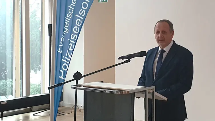 Der Redner steht hinter dem Rednerpult. Links von ihm eine Beachflag der Polizeiseelsorge mit Logo. 