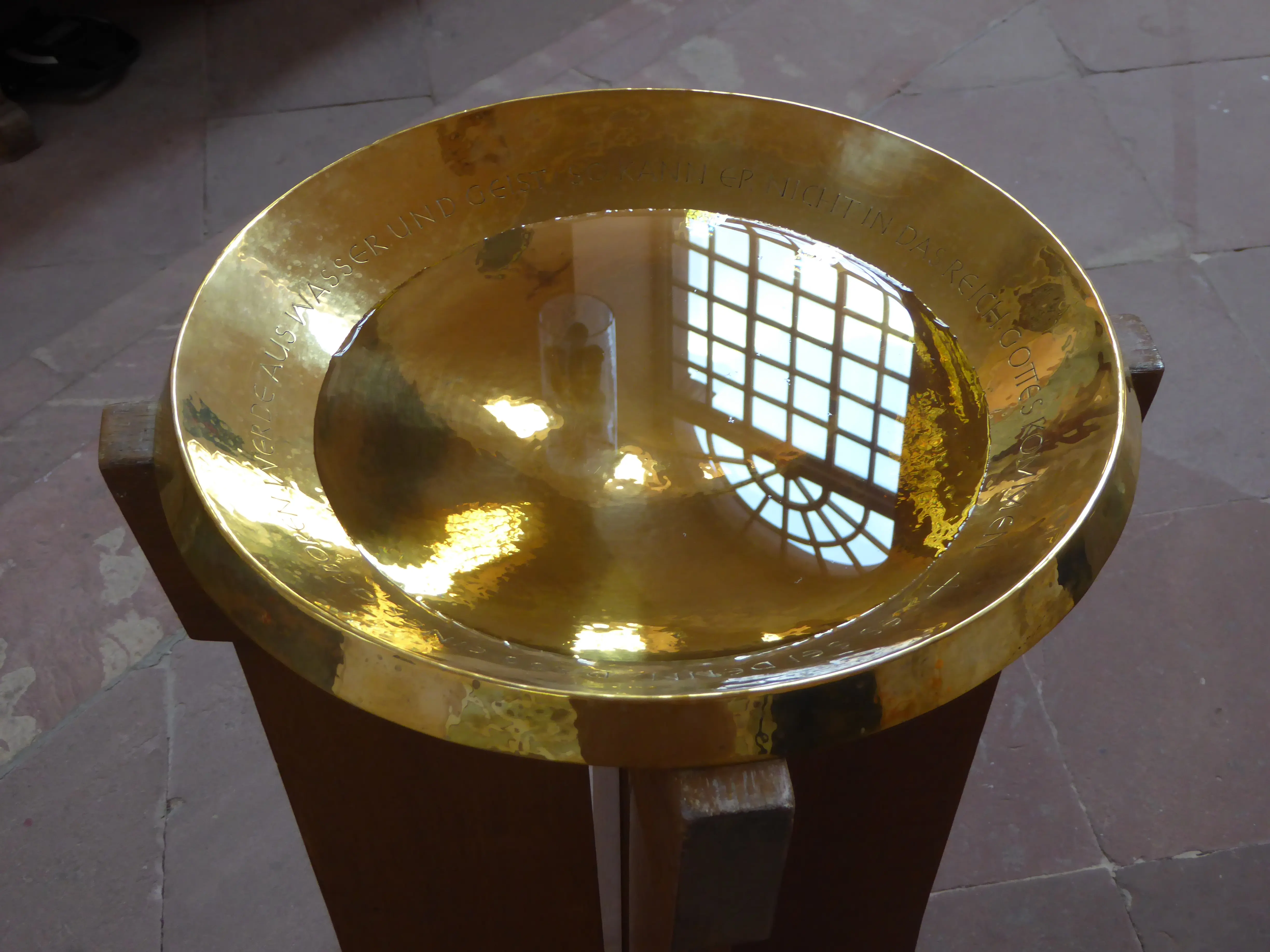 Taufschale in deren Wasser sich das Kirchenfenster spiegelt