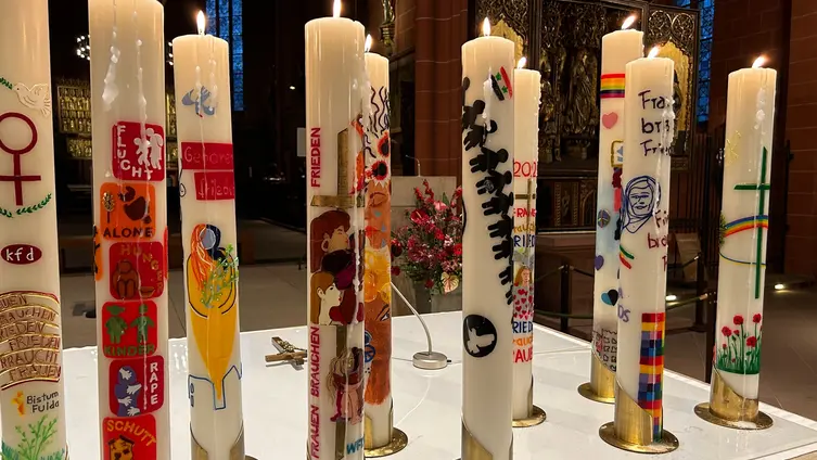 Das Bild zeigt ein Dutzend große weiße Kerzen, die bunt verziert sind.