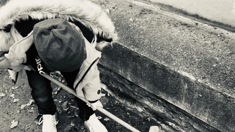 Das schwarz-weiß Foto zeigt 1 KiTa - Kind bei der "Hausmeister" - Arbeit vor der KiTa.