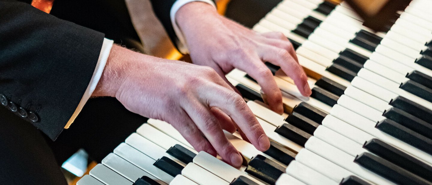 Nahaufnahme der Hände eines Organisten beim Spielen auf einer Orgel.