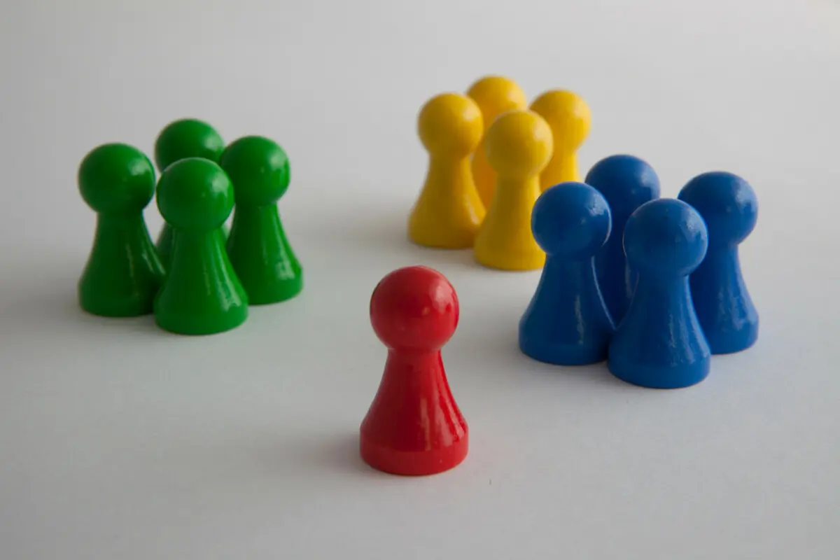 Drei Gruppen von jeweils vier grünen, blauen und gelben Spielfiguren stehen einer roten Spielfigur gegenüber