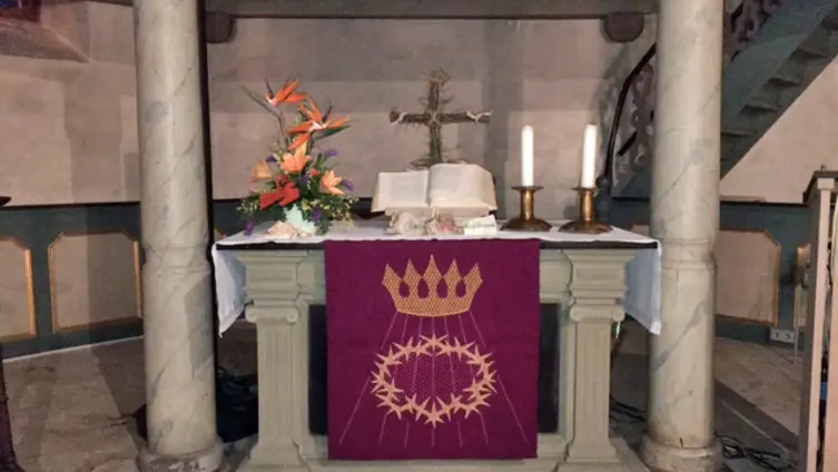 Der Altar der evangelischen Kirche Köppern mit lila Altartuch in der Passionszeit. Hinter der mittig liegenden Bibel ein aus dornigen Zweigen gebundenes Kreuz.
