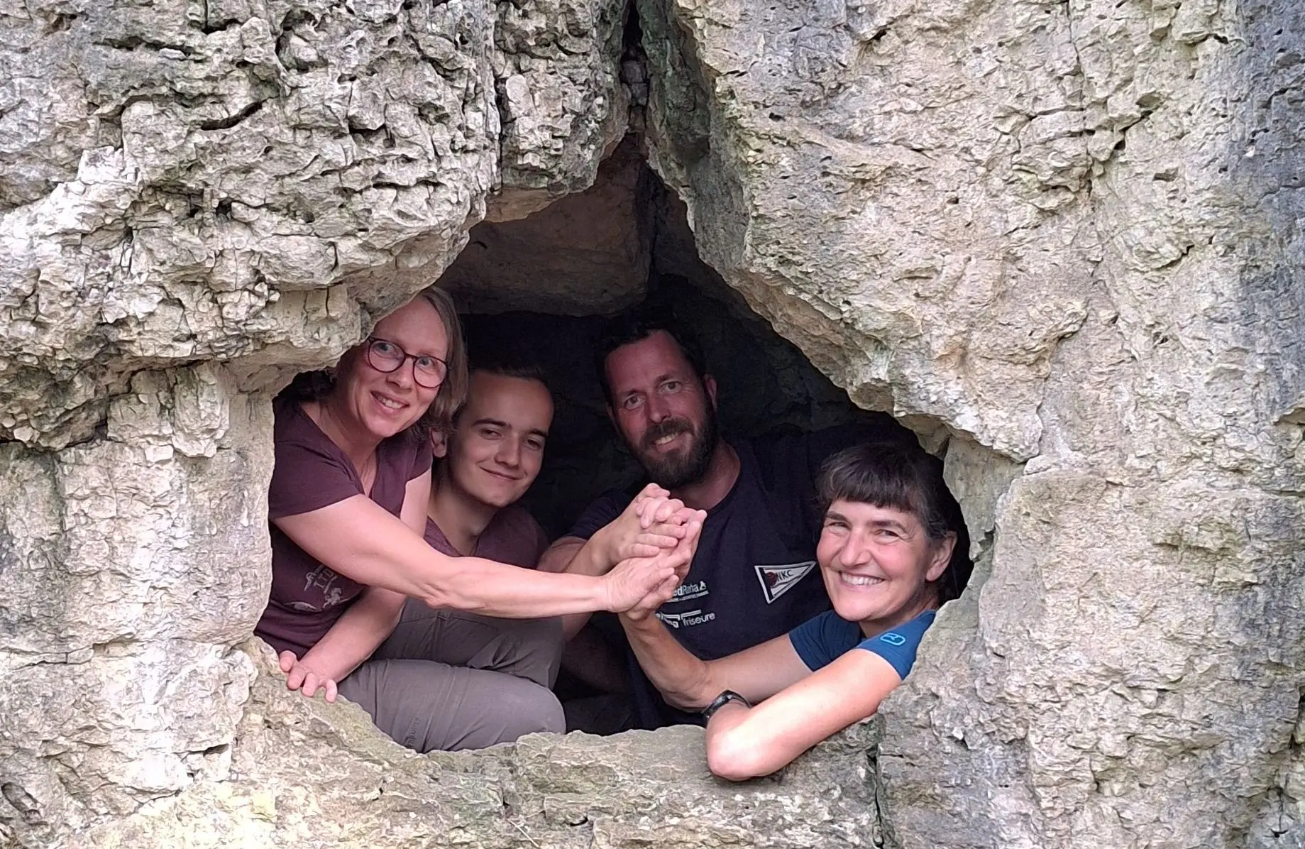 eine Gruppe Menschen schaut fröhlich aus einer Höhel durch ein Loch hinaus zur Fotografin