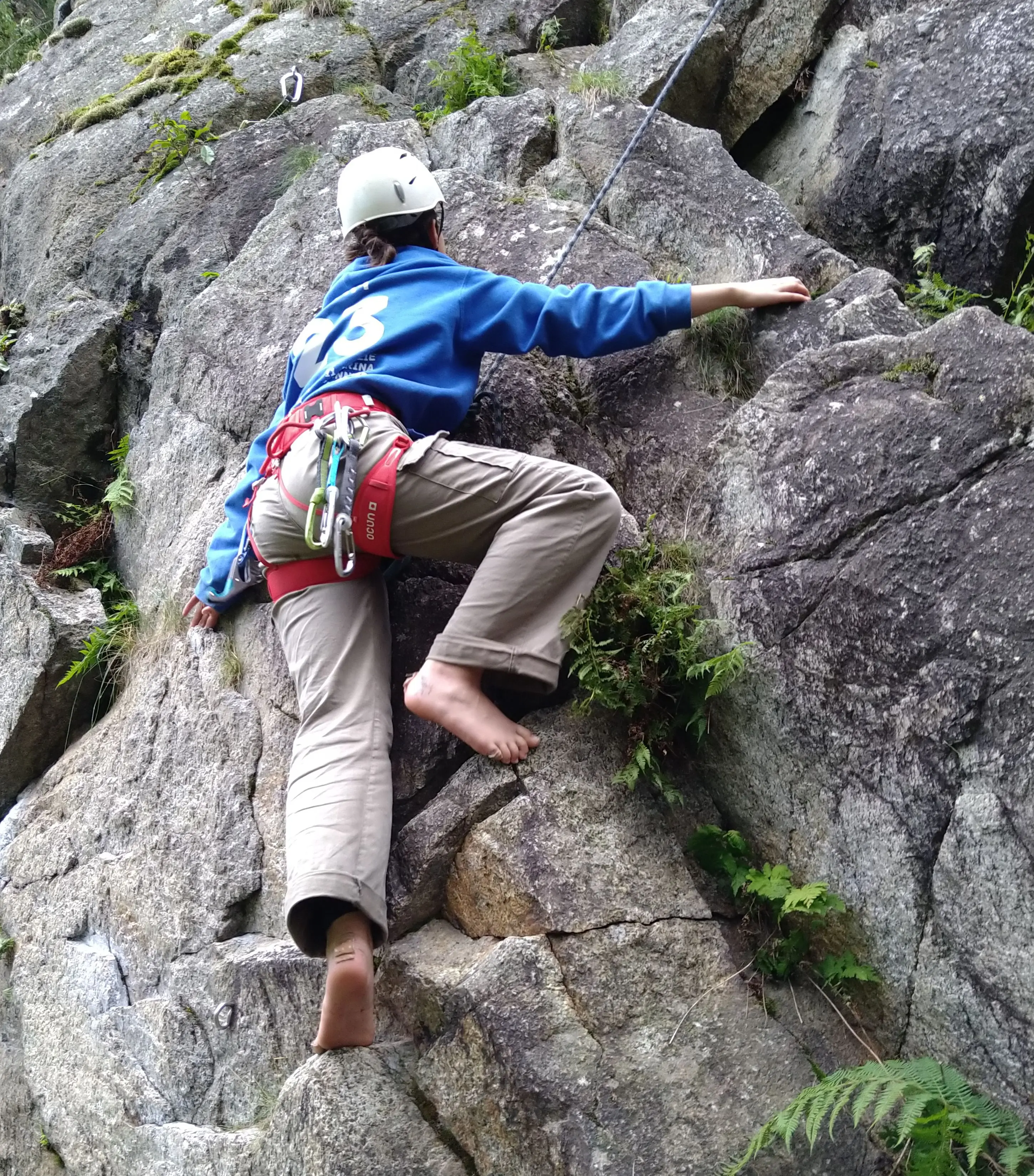 Eine Frau klettert barfuß mit Helm und Sicherungsgurt eine Felswand hoch