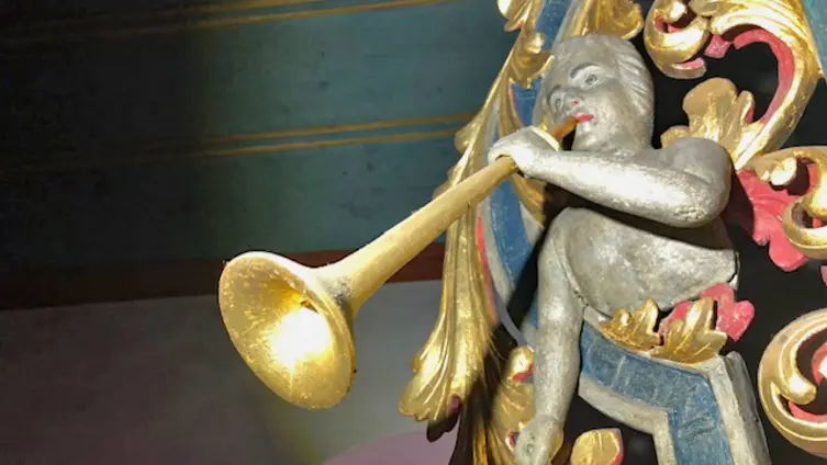 Ausschnitt mit dem nach links schauenden Posaunenengel in der linken Wange des Orgelprospekts der evangelischen Kirche Köppern. Die Posaune ragt deutlich aus der Holzverzierung heraus.