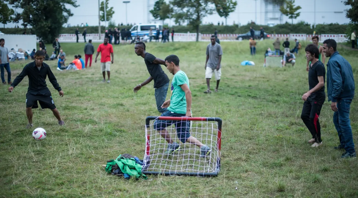 Menschen verschiedener Nationen spielen Fußball auf einer grünen Wiese.