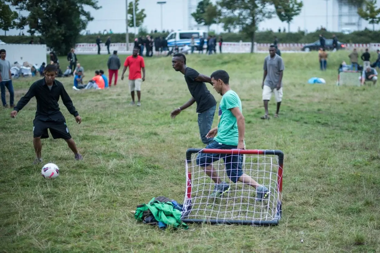 Menschen verschiedener Nationen spielen Fußball auf einer grünen Wiese.