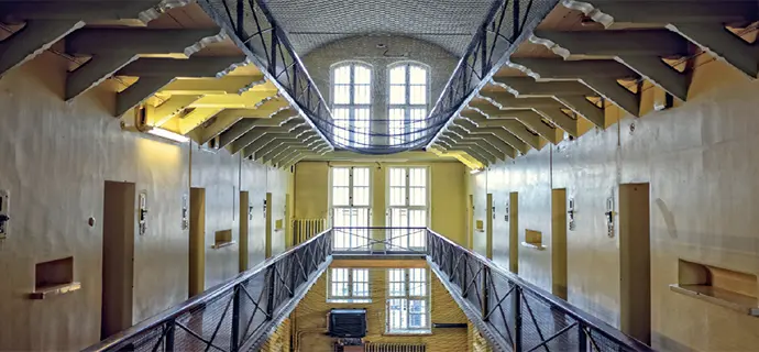 Blick durch eine alte, menschenleere Gefängnisarchitektur. Mittelachsig führen die Emporengänge
an den Zelltüren vorbei in Richtung Fenster.