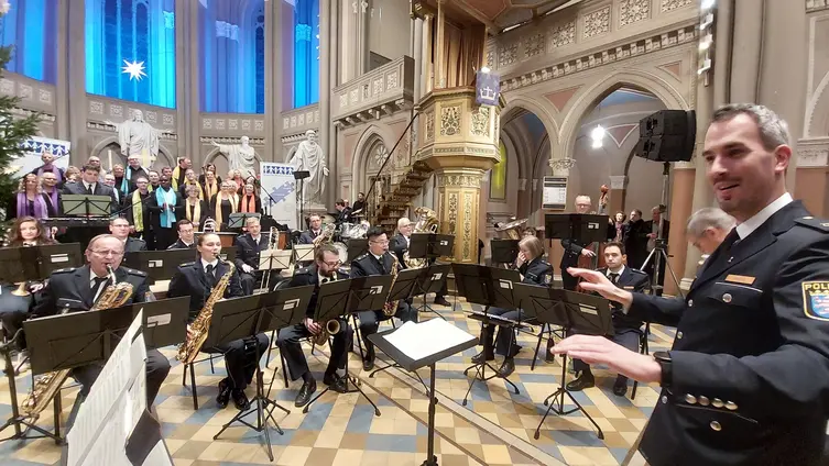 Im Altarraum sitzen die Musiker des Orchesters der Polizei. Alle tragen Uniform. Rechts im Vordergrund dirigiert Florian Weber.