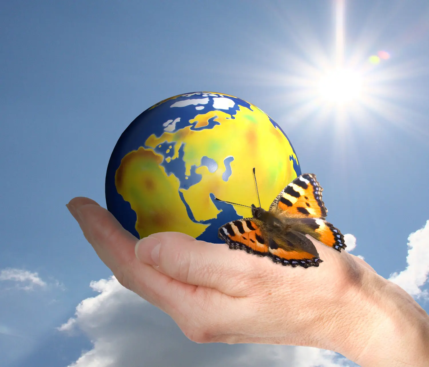 Weltkugel mit Schmetteling in einer Hand vor blauem Himmel