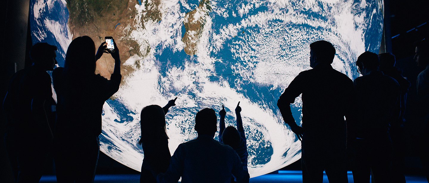 Menschen stehen vor einer illuminierten Weltkugel.