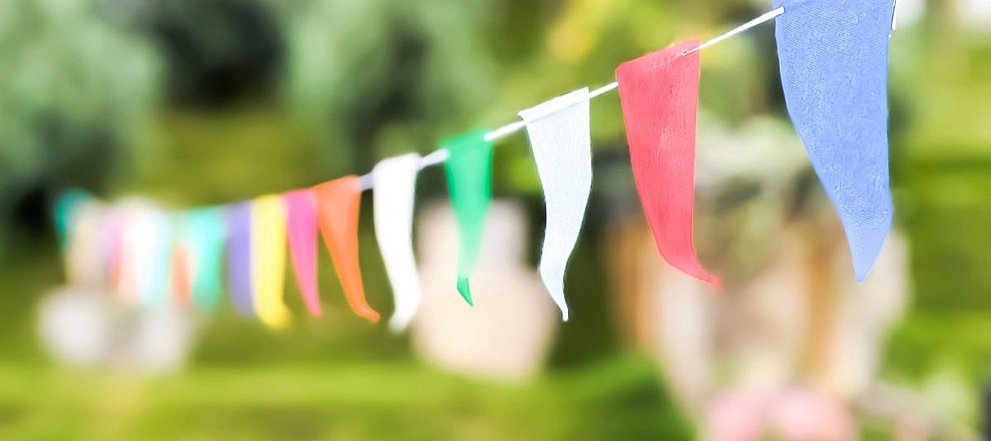 Bunte Wimpelkette vor unscharfem Gartenhintergrund