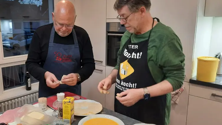 2 Personen die am Herd stehen und Essen vorbereiten