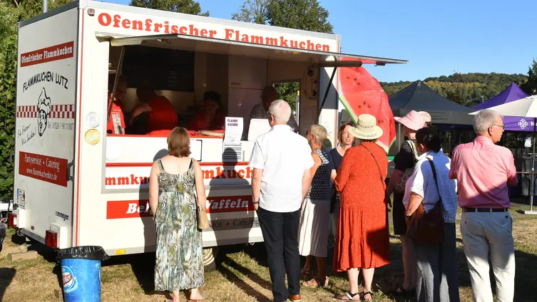 Menschen stehen vor dem Flammkuchen-Wagen an und warten auf die Ausgabe. Man sieht sie nur von hinten.