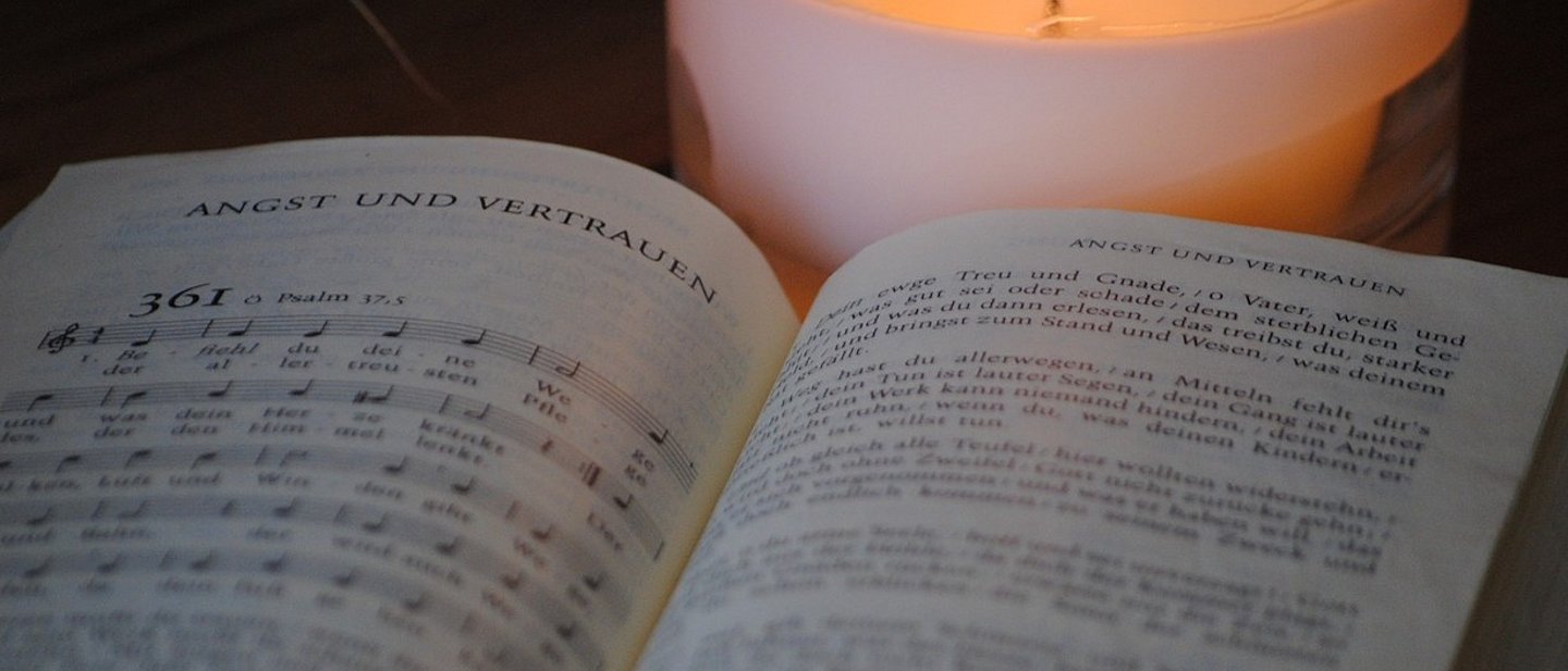 Aufgeschlagenes Evangelisches Gesangbuch mit Nummer 361; dahinter brennt eine weiße Kerze.