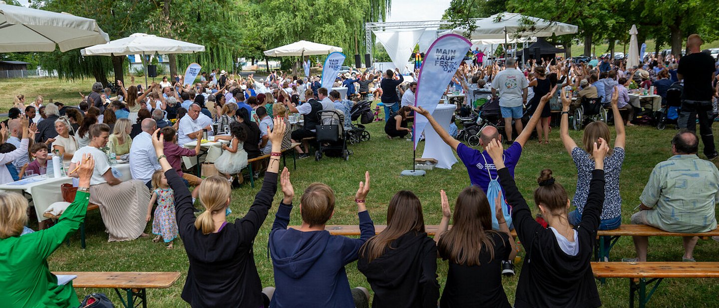 Gläubige strecken während des Gottesdienstes beim "Main Tauffest 2022" am Mainufer in Offenbach ihre Hände in die Luft.