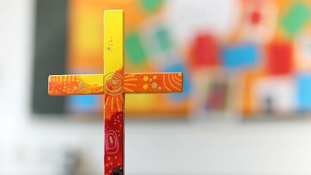 buntes Holzkreuz auf Tuch auf einem Tisch.