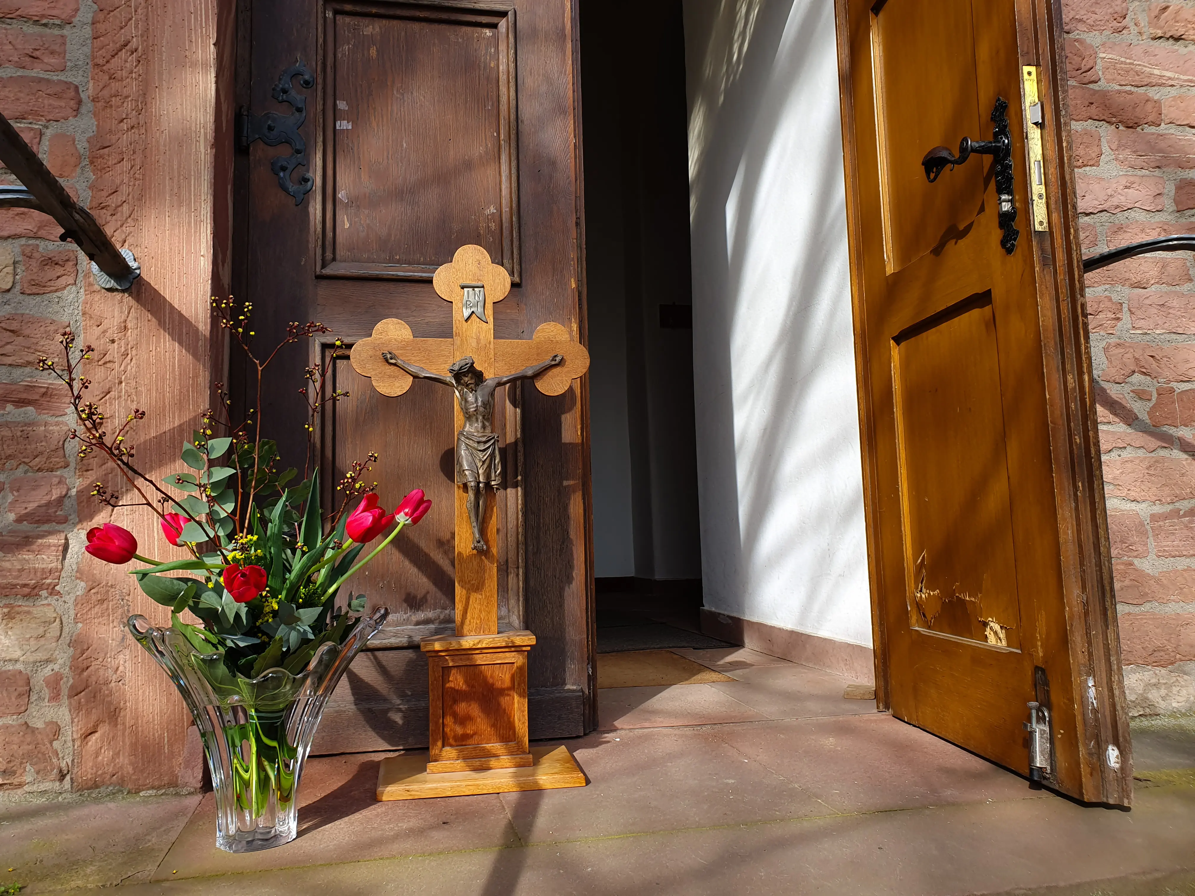 Geöffnete Eingangstür mit Blumen und Altarkreuz davor