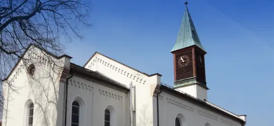 Weiße Kirche mit grünem Turmhelm und blauem Himmel im Hintergrund.