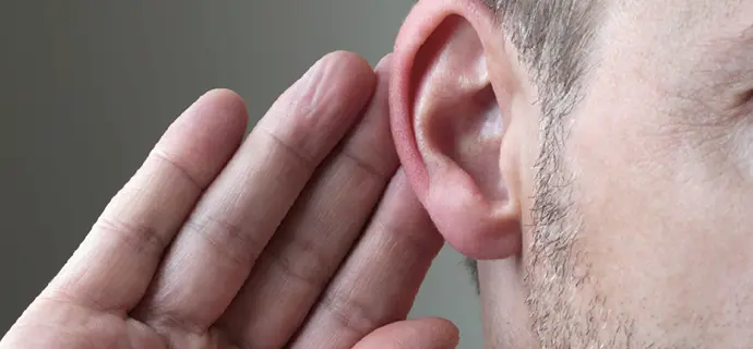 Bildausschnitt von einer Hand hinter dem Ohr als Ausdruck von Schwerhörigkeit.