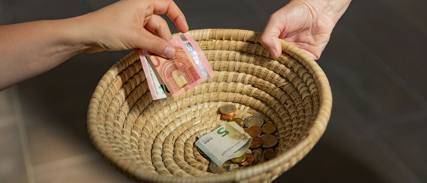 Ein geflochtenes Körbchen wird herumgereicht, um Geld einzusammeln. Ein paar Scheine und Münzen befinden sich bereits darin.