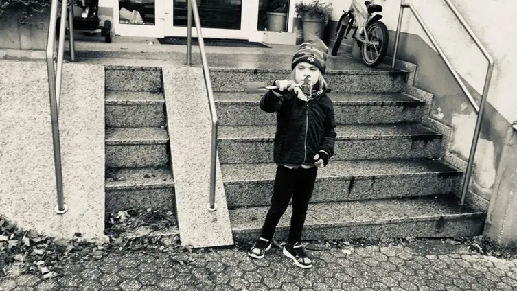 Das schwarz-weiß Foto zeigt 1 KiTa - Kind bei der "Hausmeister" - Arbeit vor der KiTa.