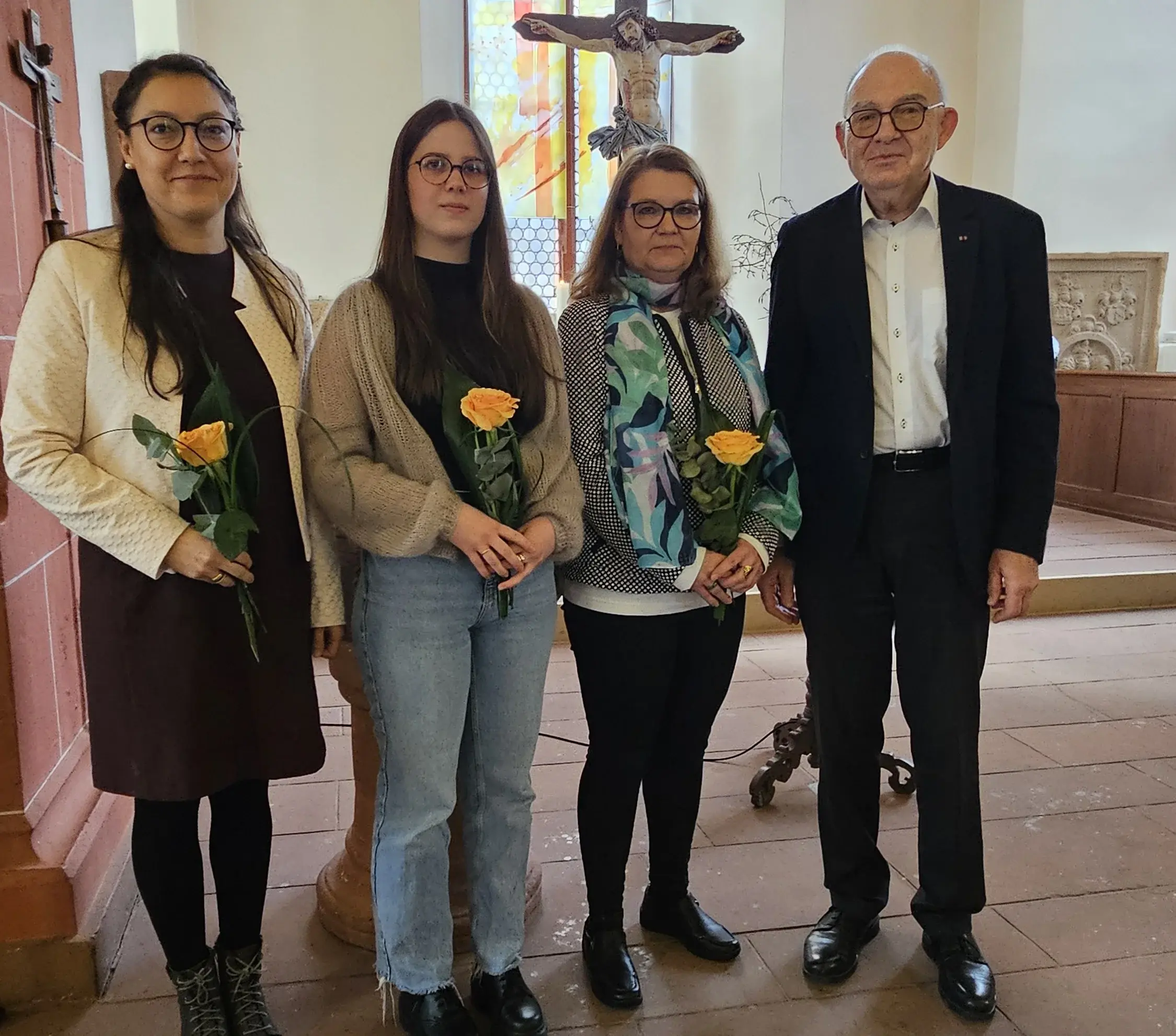 Präses Rolf Hartmann mit drei Frauen im Altarraum der Niddaer Kirche. Im Hintergrund sieht man ein Fenster, davor ein Kruz, die drei Frauen halten jeweils eine Blume in der Hand