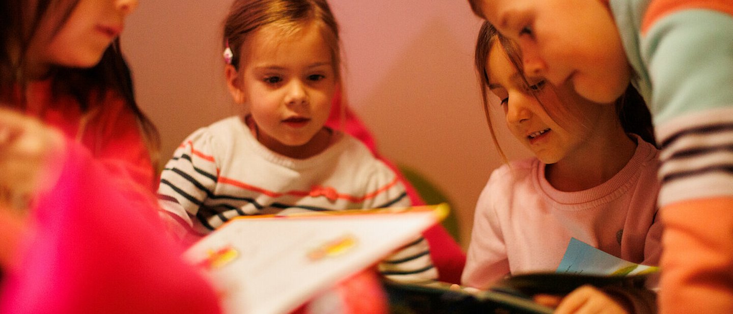 Ev. Kindertagesstätte "Kinder Garten Eden" Gemünden. Drei Mädchen und ein Junge schauen sich ein Bücher an.