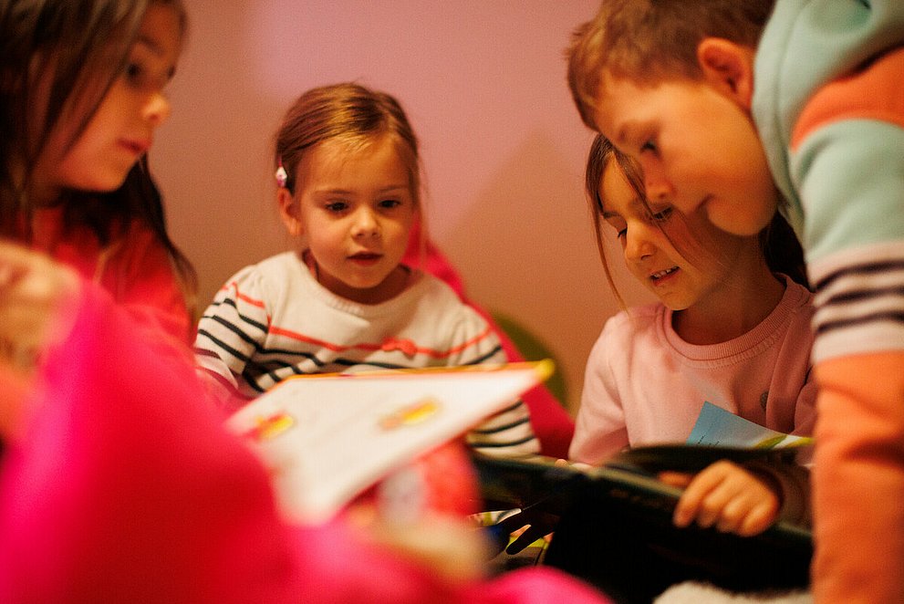 Ev. Kindertagesstätte "Kinder Garten Eden" Gemünden. Drei Mädchen und ein Junge schauen sich ein Bücher an.
