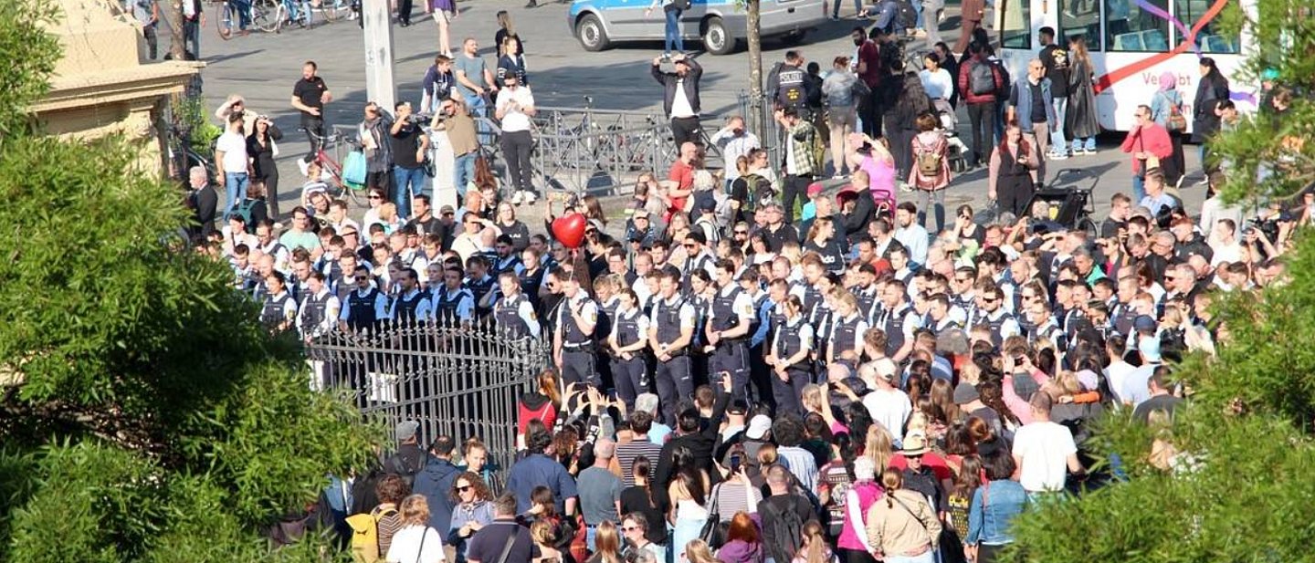 Viele Menschen versammeln sich auf einem Platz. Dabei sind viele Polzisten und Polizistinnen.